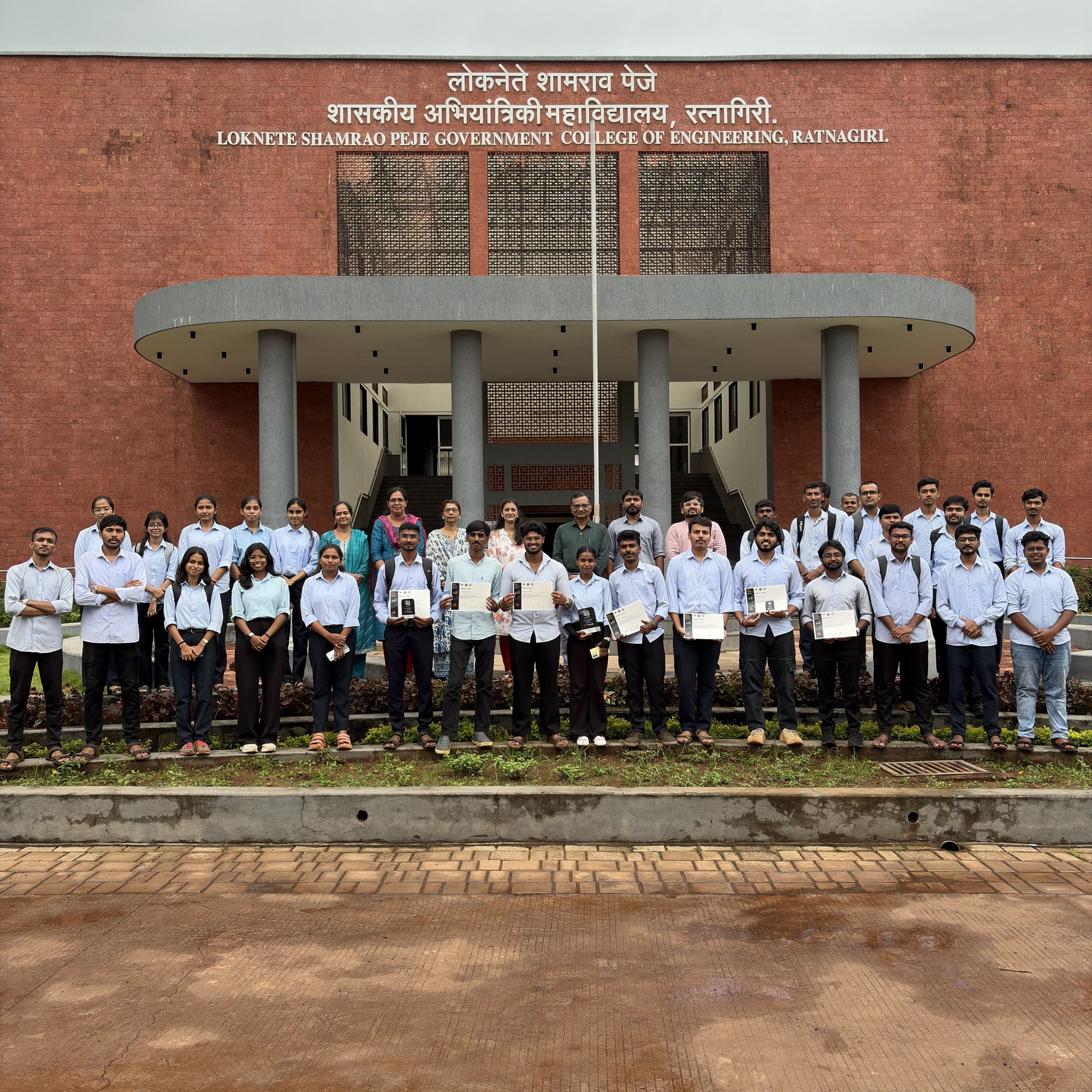 Participating students, faculty members, and Principal in front of the college building holding certificates and awards at EUREKA 2026